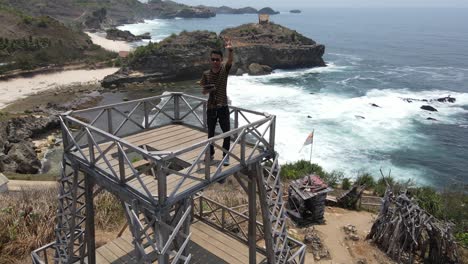 Aerial-view-of-tourists-waving-at-the-drone-and-showing-the-beautiful-Kasap-beach-located-in-Pacitan,-Indonesia