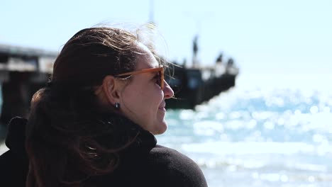 a-close-up-shoot-of-a-woman-wearing-a-hood-black-jacket-and-sunglasses-enjoying-a-sunny-and-windy-day-on-the-beach-of-Coogee,-Perth---Western-Australia