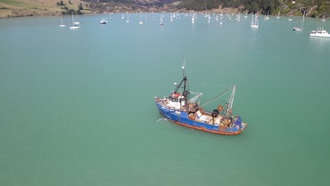 Aerial-reveal-from-fishing-ship-to-port-with-yachts-at-Banks-Peninsula,-New-Zealand-landscape