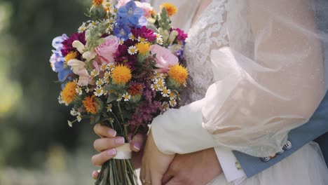 Close-up-shot-of-a-couple-holding-bouquets-in-their-hands-while-hugging-each-other---wedding-bouquet-of-fresh-rose-lupine-and-other-flowers-of-pink-and-violet-colors