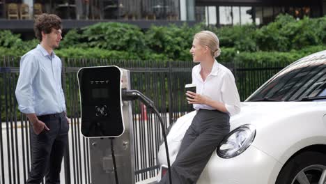Progressive-businessman-and-businesswoman-leaning-on-EV-car-and-charging-point.
