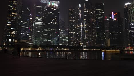 Skyline-Und-Hafenviertel-Von-Singapur-Bei-Nacht-Mit-Der-Silhouette-Von-Menschen,-Die-Vorbeigehen
