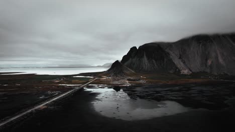 Aerial-black-sand-beach-stokksnes,-mountains,-volcanic-dark-vestrahorn-in-distance,-dark-moody-cloudy-scenery,-Iceland