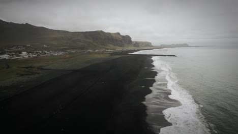 Cinematic-aerial-black-sand-beach-at-ocean-scenery,-moody-dark-scenery,-town-Vik,-Iceland
