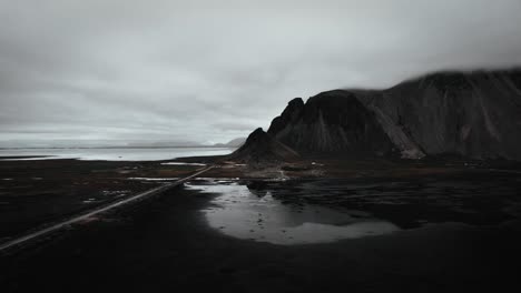 Aerial-black-sand-beach-stokksnes,-volcanic-dark-mountains-in-distance,-dark-moody-cloudy-scenery-Iceland