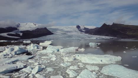 Aerial-flying-down-over-dramatic-icebergs-floating-in-water,-Jokulsarlon-lake,-winter-snow-landscape,-Iceland