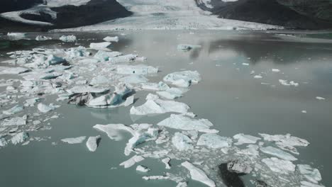 Aerial-flying-up-over-dramatic-icebergs-floating-in-water,-Jokulsarlon-lake,-natural-climate-snow-landscape,-Iceland