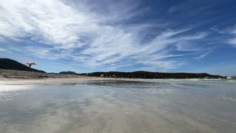 Low-angle-water-surface-view-of-people-walking-on-white-sand-of-Lotu-beach-in-summer-season,-Corsica-island-in-France