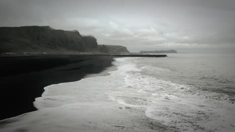 Filmische-Luftaufnahmen-Am-Schwarzen-Sandstrand,-Meereswellen,-Stimmungsvolle-Dunkle-Landschaft,-Vik,-Island