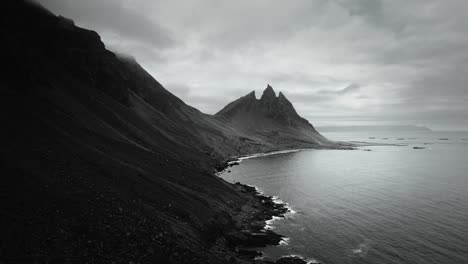 Aerial-vesturhorn-mountain,-black-sand-beach-stokksnes,-volcanic-dark-moody-cloudy-scenery,-Iceland