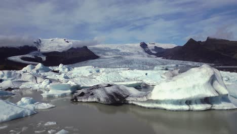 Aerial-flying-over-dramatic-icebergs-floating-in-water,-Jokulsarlon-lake,-winter-snow-landscape,-Iceland