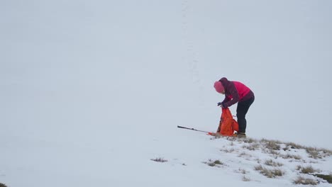 Woman-in-pink-coat-and-hat-checking-equipment-while-standing-in-snow