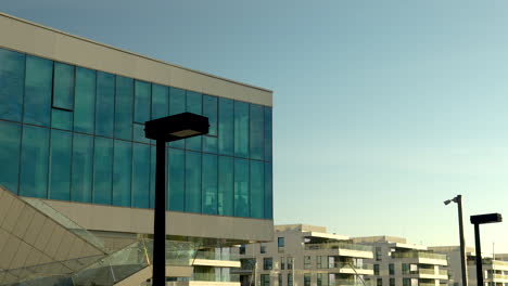 Modern-glass-building-with-blue-sky-reflection,-street-lamps-in-urban-setting-at-dusk
