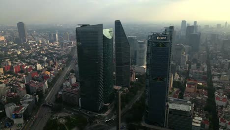 Descending-aerial-orbit-with-glass-buildings-at-the-beginning-of-Paseo-de-la-Reforma-at-dusk-with-fog,-Mexico-City