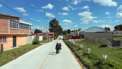 Dolly-in-a-group-of-three-girls-walking-in-the-middle-of-a-new-road-in-the-rural-area-of-Almoloya,-State-of-Mexico