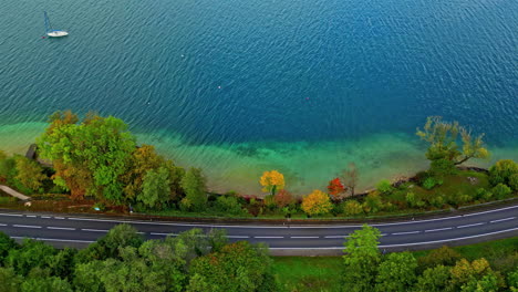 Aerial-overview-of-a-car-on-a-road-on-the-coast-of-lake-Attersee,-fall-in-Austria