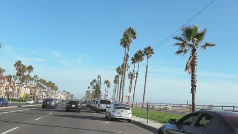 Huntington-Beach-street-with-palm-trees,-cars,-houses-and-promenade