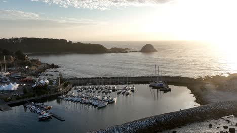 Aerial-Shot-of-Harbor-with-Sailing-Boats-with-Peña-Blanca-Islet,-Pacific-Ocean,-in-the-distance-at-Sunrise-or-Sunset-in-Chile,-South-America