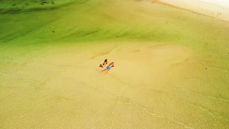 Orbital-aerial-drone-shot-of-two-tourists-lying-on-a-sand-bar,-surrounded-by-shallow-waters-in-Choeng-Mon-beach-in-the-island-of-Koh-Samui-in-Surat-Thani-province-in-Thailand