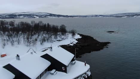 Vista-De-Drones-En-Tromso-Volando-Hacia-El-Mar-Desde-Una-Zona-Nevada-Con-Montañas-Llenas-De-Nieve-En-Invierno-En-Noruega