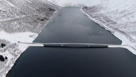 Drohnenansicht-In-Der-Gegend-Von-Tromsø-Im-Winter-Beim-Flug-über-Einen-Fjord,-Umgeben-Von-Weißen-Bergen-Und-Einer-Brückenüberquerung-In-Norwegen