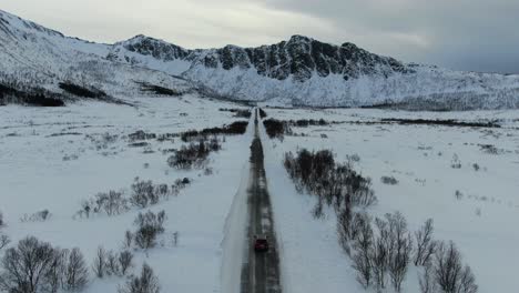 Vista-De-Drones-En-La-Zona-De-Tromso-En-Invierno-Volando-Sobre-Una-Carretera-Estrecha-En-Medio-De-Un-Paisaje-Nevado-Siguiendo-Un-Coche-Desde-Arriba-En-Noruega