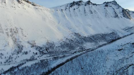 Vista-De-Drones-Sobre-Las-Montañas-De-Tromso-En-Invierno-Llenas-De-Nieve-Que-Muestra-Un-Bosque-Desde-Arriba-En-Noruega-Volado-De-Lado