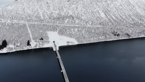 Drohnenansicht-In-Der-Gegend-Von-Tromsø-Im-Winter-Beim-Flug-über-Einen-Fjord,-Umgeben-Von-Weißen-Bergen-Und-Einer-Brückenüberquerung-In-Norwegen