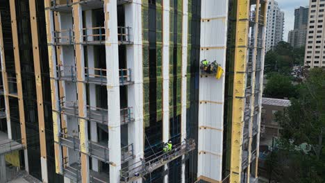 Vista-Aérea-Que-Muestra-A-Un-Trabajador-En-Un-Ascensor-Trabajando-En-Un-Sitio-De-Construcción-De-Rascacielos-En-La-Ciudad-De-Atlanta.