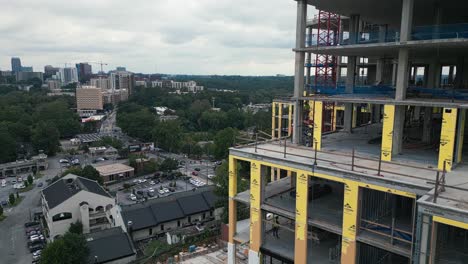 Ascending-drone-shot-of-worker-checking-skyscraper-construction-site-with-large-crane-and-traffic-on-highway-in-suburb-area-of-Atlanta-City