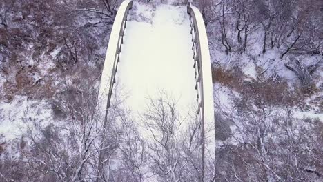 Winter-snow-flyover-of-long-abandoned-bridge-over-small-frozen-river