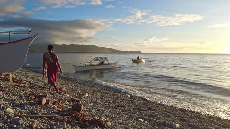 Cinematic-shot-of-topless-Filipino-fishermen-coming-into-shore-on-small-kayak-style-fishing-boats-during-golden-hour