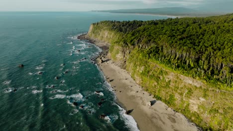 Aerial-view-of-stunning-rocky-and-rugged-peninsula-landscape-with-windswept-forest-of-trees,-Bruce-Bay-in-South-Westland,-New-Zealand-Aotearoa