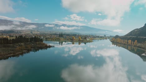 Vista-Aérea-Panorámica-De-Un-Tranquilo-Y-Reflexivo-Lago-Dunstan-Con-Nubes-En-La-Superficie-Del-Agua-En-La-Ciudad-De-Cromwell-En-La-Región-Central-De-Otago-En-La-Isla-Sur,-Nueva-Zelanda-Aotearoa