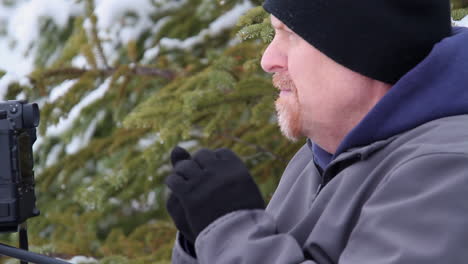 Cold-winter-male-photographer-in-conifer-forest-warms-gloved-hands