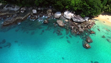 Drone-video-of-4-people-snorkelling-near-huge-granite-stones,-white-sandy-beach,-turquoise-transparent-Indian-ocean-water,-Mahe,-Seychelles-30fps