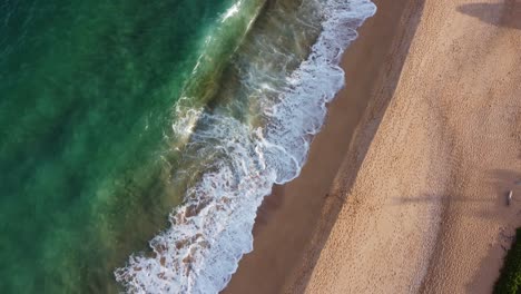 Aerial-top-down-view-over-clear,-transparent-ocean-water-foaming-at-the-shore