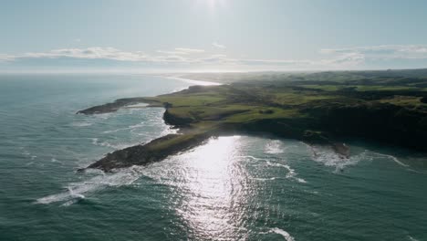 Stunning-aerial-view-of-the-southernmost-point-of-the-South-Island-of-New-Zealand-Aotearoa,-with-beautiful-hazy-sunlight,-ocean-views-and-scenic-rugged-coastline