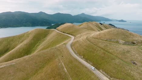 Aerial-drone-view-of-white-campervan-on-road-trip-traveling-along-a-remote-road-exploring-the-Te-Aumiti-French-Pass-region-of-Marlborough-Sounds,-South-Island-of-New-Zealand-Aotearoa