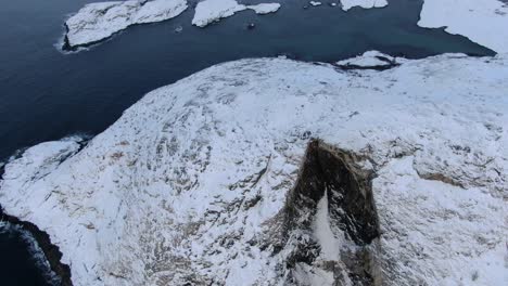 Drone-view-in-Tromso-area-in-winter-flying-over-a-snowy-mountain-peak-surrounded-by-the-ocean-in-Norway