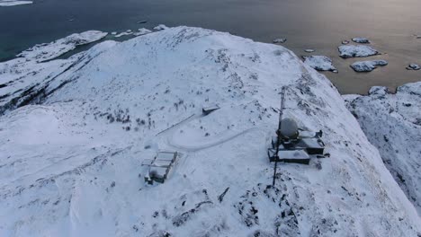 Drone-view-in-Tromso-area-in-winter-flying-over-a-snowy-mountain-peak-and-into-the-ocean-in-Norway