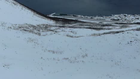 Vista-De-Drones-En-La-Zona-De-Tromso-En-Invierno-Volando-Sobre-Una-Montaña-Nevada-Y-Mirando-Hacia-El-Fiordo-En-Segla,-Noruega