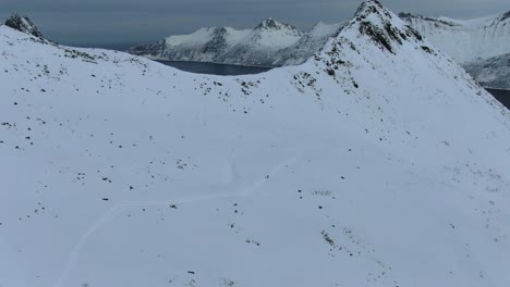 Drohnenansicht-In-Der-Gegend-Von-Tromsø-Im-Winter-über-Einem-Schneebedeckten-Berg-In-Segla,-Norwegen,-Mit-Dem-Meer-Am-Horizont
