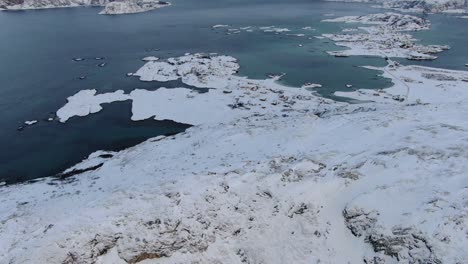 Vista-De-Drones-En-La-Zona-De-Tromso-En-Invierno-Volando-Sobre-Un-Pico-Nevado-De-Montaña-Con-El-Mar-En-El-Horizonte-En-Noruega