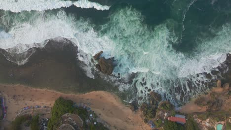 Sliding-overhead-drone-shot-of-coastline-with-tidal-wave-moving-toward-to-the-beach