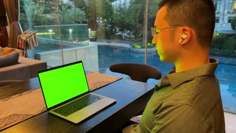 Wohlhabender-Asiatischer-Millennial-Sitzt-In-Einem-Luxushaus-Und-Schaut-Sich-Einen-Laptop-Mit-Grünem-Bildschirm-An