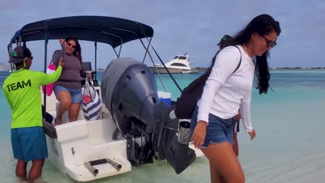 Two-latin-women-getting-off-motorboat-on-beach-helped-by-the-boat-crew-men,-caribbean