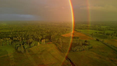 Rainbow-after-rain-above-rural-field-landscape,-Aerial-view