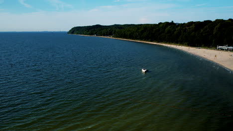 Aerial-view-of-boat-on-Baltic-Sea-with-forest-landscape-and-sandy-beach-in-Gdynia-,-Poland