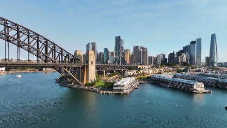 Retirada-Aérea-Desde-La-Vista-Del-CDB-De-Sydney-Para-Revelar-El-Puente-Del-Puerto-De-Sydney-Mientras-El-Ferry-Pasa-Al-Atardecer,-Australia